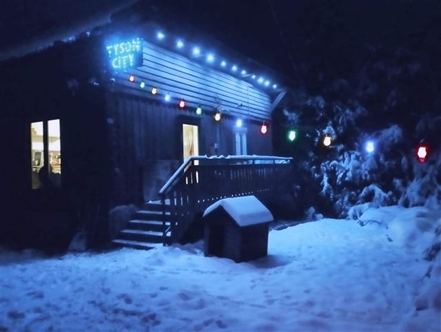 Chalet Tyson City illuminé la nuit sous la neige avec enseigne LED et guirlandes